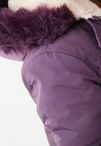 Doudoune violette avec une capuche en fourrure blanche et duveteuse, un extérieur lisse et des coutures visibles le long des seams.