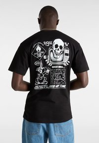 Camiseta negra de manga corta con estampados gráficos en blanco en la parte posterior, que presenta una calavera, un televisor, un conejo y elementos de texto. Material de algodón, corte relajado.
