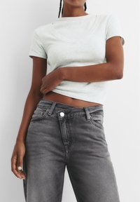 T-shirt aderente grigio chiaro con scollo a barca, abbinato a jeans a vita alta grigio scuro. Tessuto morbido, dettagli di cucitura minimi.