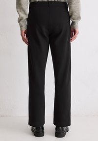 Pantalon noir sur mesure en tissu doux, doté d'une coupe droite, de poches arrière et d'une taille lisse.
