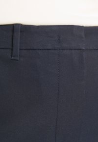 Mörkblå byxor med en slät textur, med rak passform, bälteshällor och subtila sömnadsdetaljer längs sömmarna.