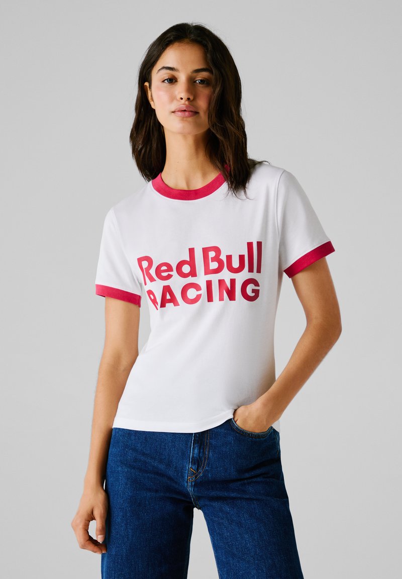 Tricou alb cu maneci scurte, guler și margini de manșetă roșii, având un imprimeu îndrăzneț "Red Bull RACING" în roșu. Material din bumbac, croială casual.