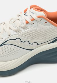 Baskets légères avec une tige en maille crème, des accents orange et des détails bleus. Présente une surface texturée et une semelle rembourrée.