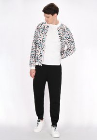 Giacca bomber da uomo con un motivo maculato multicolore, t-shirt bianca, pantaloni neri e sneakers bianche. Presenta polsini elasticizzati e una vestibilità comoda.