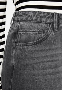 Graue Denim-Jeans mit Nahaufnahme des Bundes und der Tasche, die eine weiche, strukturierte Oberfläche und subtile Nähte aufweisen.