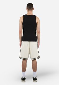 Svart ermeløs tanktop med et teksturert mønster, parret med kremfargede shorts med svart kant og elastisk midje. Hvite sokker og sko.