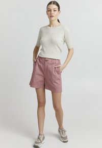 Strikket kremfarget topp med ribbet tekstur, parret med lyse rosa shorts med knapp og elastisk liv. Grå og beige joggesko.