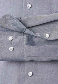 Jasnoszara koszula z guzikami, wykonana z teksturowanej tkaniny, z białymi guzikami i złożonym mankietem. Dwa zapięcia na guzik na mankiecie.