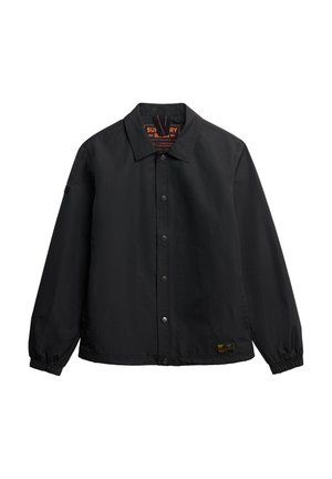Chaqueta negra con cuello tipo solapa, cierre de botones a presión, puños elásticos y una etiqueta impresa en el interior. Textura de tela suave.