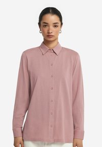 Långärmad rosa skjorta med knappar, tillverkad av mjukt tyg med krage, och har en rak skärning och knäppning fram.