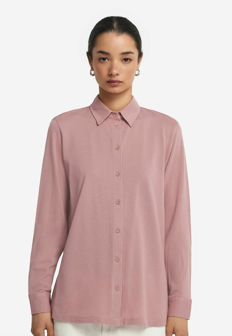 Långärmad rosa skjorta med knappar, tillverkad av mjukt tyg med krage, och har en rak skärning och knäppning fram.