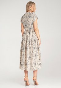 Hellbeiges Blumenkleid mit kurzen Ärmelchen, taillierten Taille und gestuftem Rock, verziert mit navyblauen Blumenmustern. Getragen mit Scherpen Sandalen.