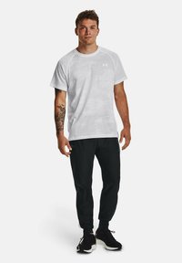 Witte sportieve T-shirt met een textuurpatroon, gedragen met zwarte tapered broek en zwarte sneakers. Heeft een logo op de borst.