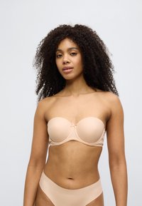 Nudetone stroppeløs BH med formpressede kopper, mykt stoff, blonderand og en liten sløyfedetalj i midten; kombinert med matchende undertøy.