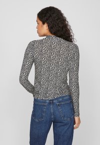 Top à manches longues avec un col montant, présentant un motif abstrait noir et blanc, fabriqué dans un tissu lisse et extensible. Porté avec un jean bleu.