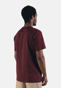 Bordeauxfarbene Baumwoll-T-Shirt mit kurzen Ärmeln und Rundhalsausschnitt, mit einem lockeren Schnitt und glatter Textur, von hinten betrachtet.