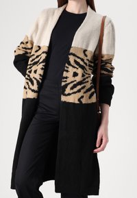 Długi kardigan w kolorach blokowych: kremowy, beżowy i czarny. Tekstura z wzorem tygrysich pasków na rękawach.