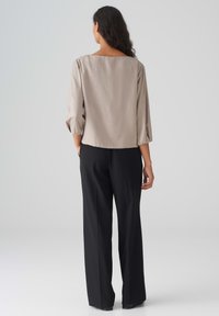 Beige, strukturierte Bluse mit weitem Rundhals und drei Viertelärmeln, kombiniert mit schwarzen, maßgeschneiderten Hosen in geradem Schnitt.