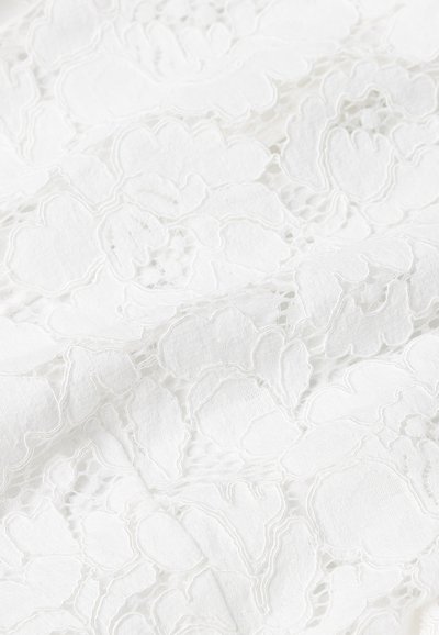 Witte kantstof met bloemmotieven en een gestructureerd oppervlak. Het ontwerp bevat ingewikkelde opengewerkte details en een zachte afwerking.