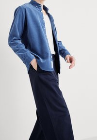 Chemise boutonnée en velours côtelé bleu avec col, manches longues et coupe décontractée, associée à un pantalon large bleu marine foncé.
