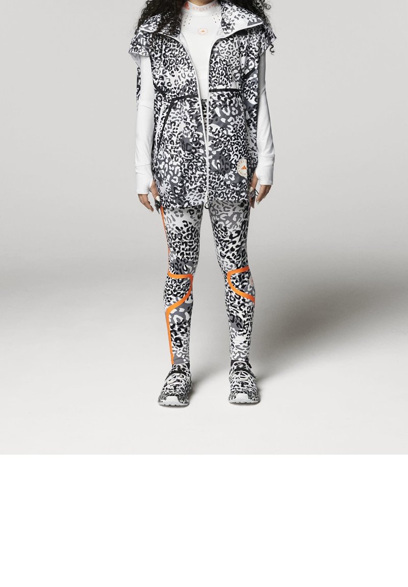 Svart-vitt leopardmönstrat träningslinne med dragkedja, kombinerat med matchande leggings med orange detaljer och texturerad tyg.