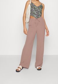 Haut court noir à fleurs avec col en V, pantalon rose pâle à jambes larges et sandales blanches à lanières, présentant un tissu doux et une coupe décontractée.
