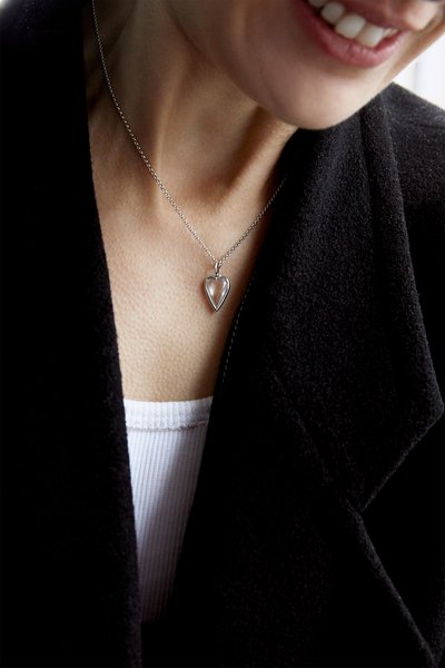 Silver necklace with a heart-shaped pendant, featuring a sleek design, smooth texture, and delicate chain resting on a collarbone.