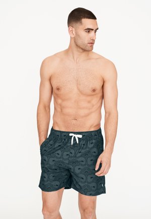 Herren Badehosen in Dunkelgrün mit einer kontrastierenden weißen Kordel. Sie verfügen über ein gemustertes Design, einen elastischen Bund und Seitentaschen.