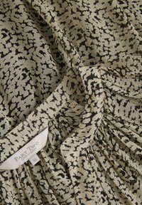 Tissu léger avec un fond beige présentant un motif abstrait noir. Comprend une étiquette avec "Part Two" et une taille 36. Détail de conception plissé.