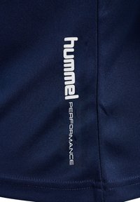 Tkanina w kolorze granatowym z pionowym białym logo "hummel PERFORMANCE" nadrukowanym w pobliżu przeszytego szwu.