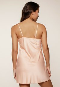 Abito a camicia in satin rosa chiaro con spalline sottili e regolabili, texture liscia e orlo corto, progettato per una silhouette aderente e fluida.