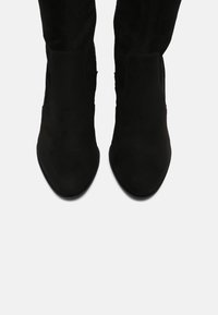 Černé semišové kotníkové boty s hladkým povrchem, špičatou špičkou a minimalistickým designem; elastické boční panely pro snadné obouvání.