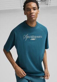 Mėlynos spalvos sportinė marškinė, pagaminta iš minkštos medžiagos, su trumpomis rankovėmis, su išsiuvinėtu kontrastingos spalvos "Sportswear by Puma" logotipu.