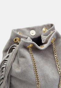 Borsa a secchiello grigia in suede con manici a catena color oro e occhielli. Chiusura con laccetto nella parte superiore e dettagli frangiati su un lato.