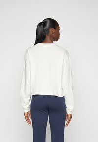 Kuttet langermet sweatshirt i off-white bomull med rund hals og ribbestrikkede mansjetter, sammen med navy leggings.