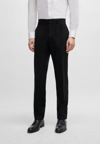 Black tailored trousers with a slim fit, made of smooth fabric. Features a flat front, belt loops, and side pockets. Worn with a white shirt.