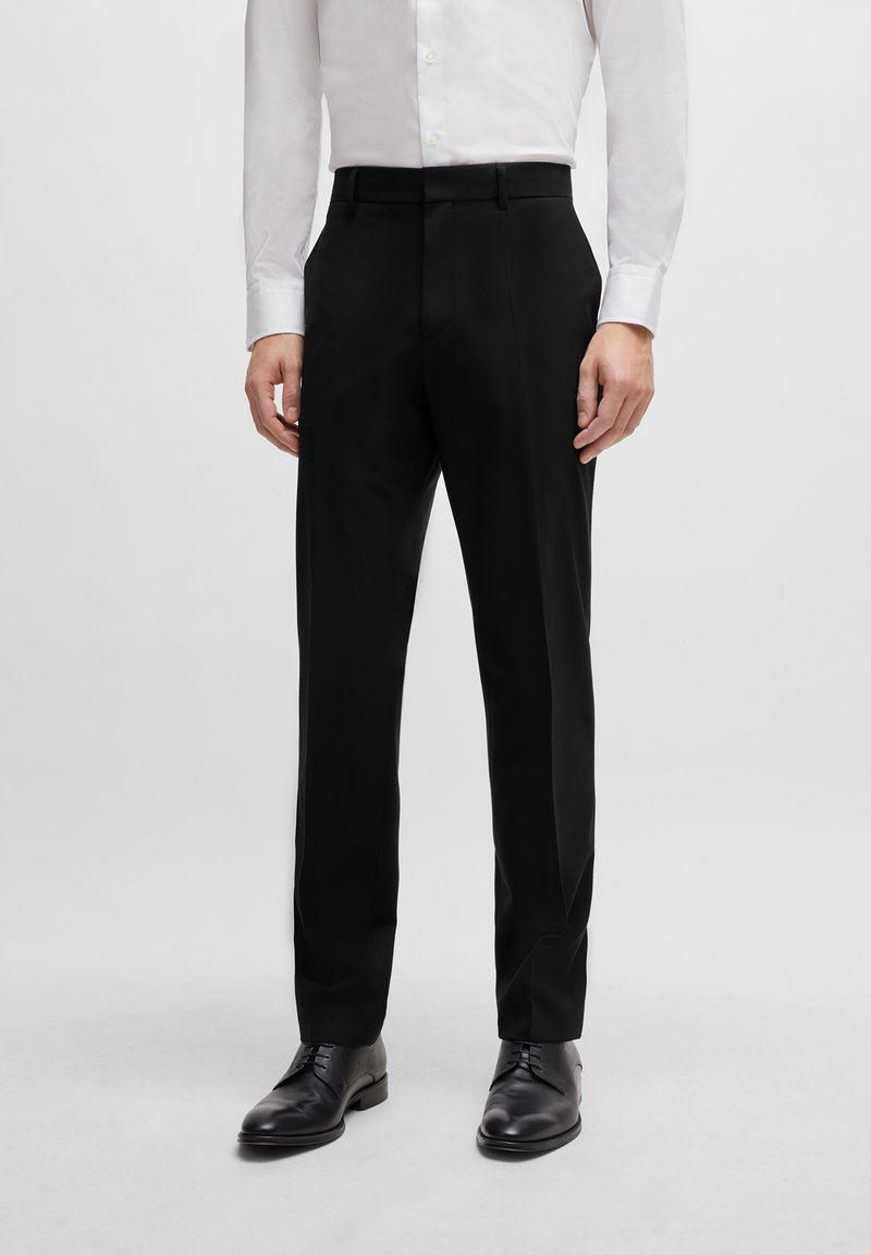Black tailored trousers with a slim fit, made of smooth fabric. Features a flat front, belt loops, and side pockets. Worn with a white shirt.