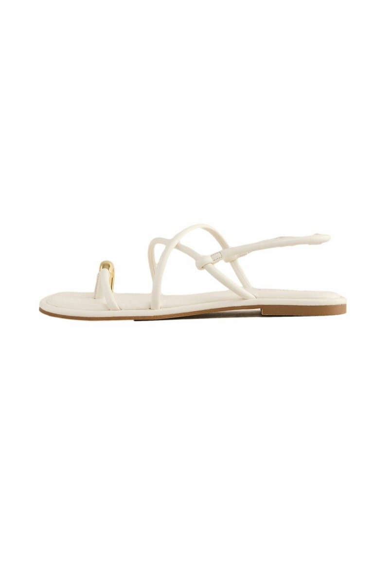 White flat sandals with thin, crisscross straps, a toe loop, a minimalistic design, and a brown rubber sole. Features a small gold accent.