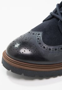 Námořnické kožené a semišové boty s brogue detaily, kulatou špičkou a hnědou gumovou podrážkou s drsným povrchem.