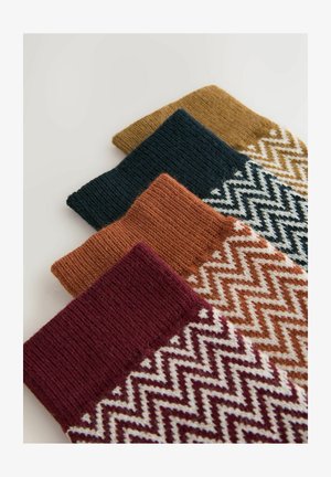 Sæt af fire strikkede sokker i mørkegrøn, sennepsgul, brændt orange og burgunder; med et zigzag-mønster på den nederste del.