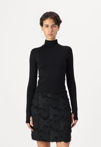Black turtleneck top in a fitted design, paired with a black skirt featuring textured floral patterns and fringed accents.