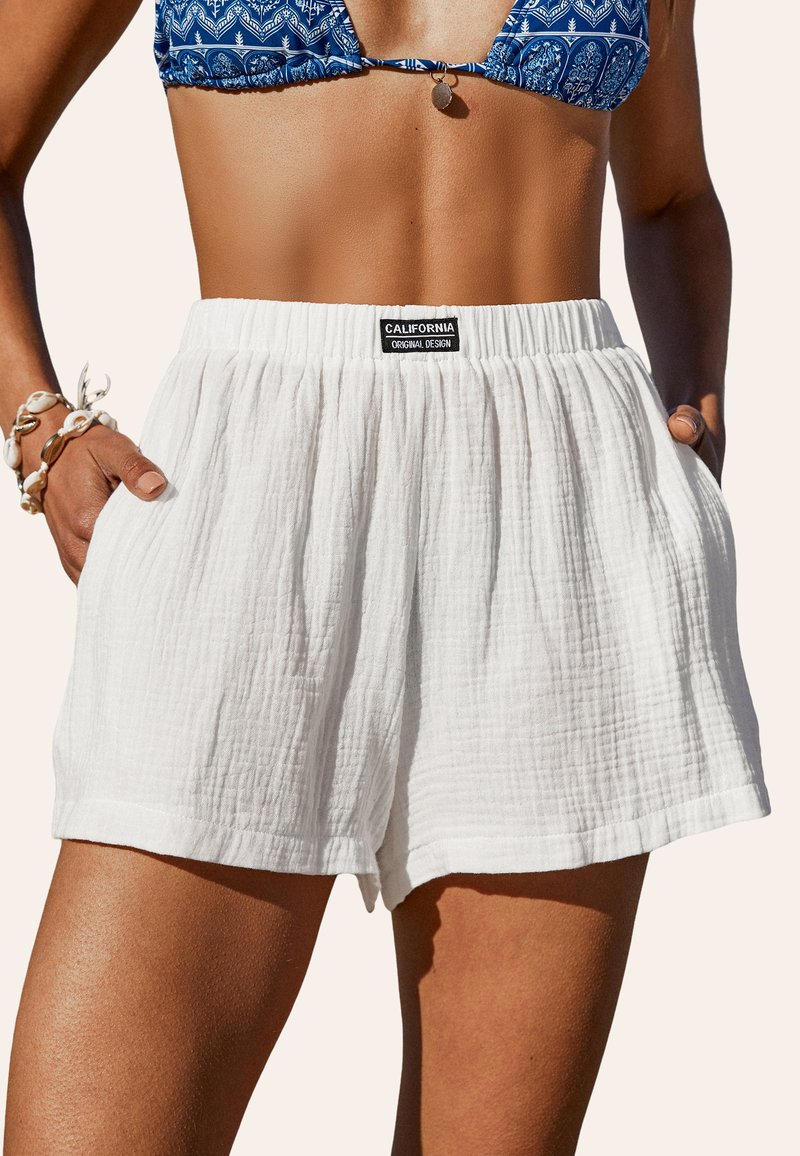 Shorts blancs texturés avec une taille élastique et des poches latérales. Présente une étiquette noire portant l'inscription « CALIFORNIA ORIGINAL DESIGN. »
