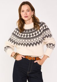 Maglione lavorato a maglia in crema con un collo patito grigio, maniche lunghe, polsini a coste e un collo aderente, abbinato a jeans scuri e una cintura marrone.