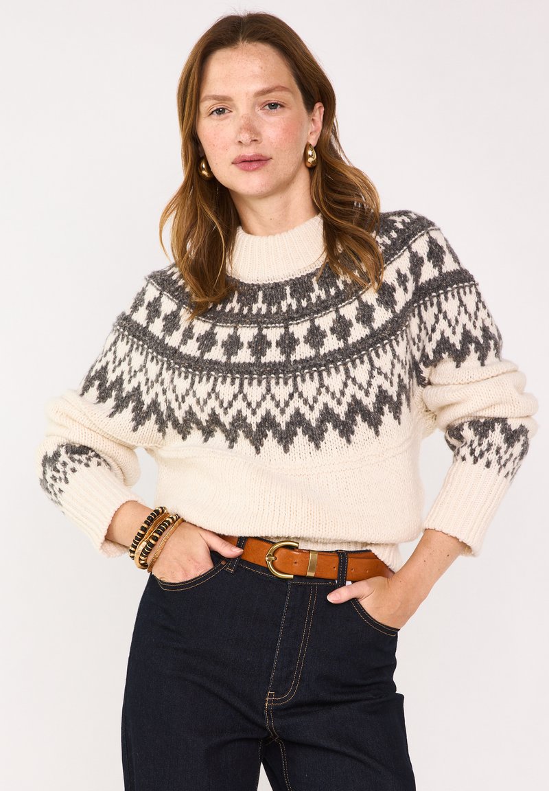 Maglione lavorato a maglia in crema con un collo patito grigio, maniche lunghe, polsini a coste e un collo aderente, abbinato a jeans scuri e una cintura marrone.