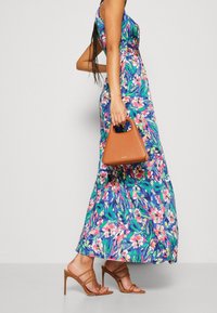 Maxi-mekko kukkakuosisessa kankaassa, jossa on sinisiä, vihreitä ja vaaleanpunaisia kuvioita. Mekossa on istuva yläosa ja virtaava hame. Mukana kolmiomainen ruskea käsilaukku.