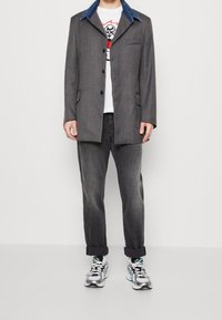 Grå blazer med denimkrage, enkel bröstficka och skarpa slag, i kombination med blekt grå jeans och metalliska sneakers.