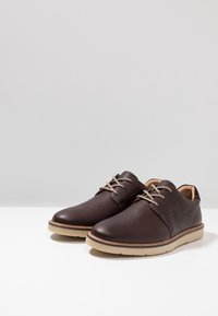 Chaussures en cuir marron avec une finition texturée, bout rond et lacets gris. Dotées d'une semelle de couleur claire et d'un design simple et classique.