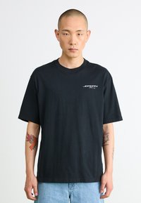 Black cotton t-shirt with a crew neck and short sleeves, featuring a small white graphic on the chest. Casual fit, smooth texture.