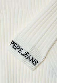 Balta raukinė su juodu "PEPEJEANS" logotipu ant rankovės. Audinys turi tekstūruotą paviršių su ryškiomis vertikaliomis linijomis.