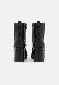 Mustat nahkasaappaat nilkkamittaisella varrella, neliönmuotoisella kärjellä, korkea blokki-korko ja takavetoketju. Sisältää ompelutaiat ja kangaspaneelit.